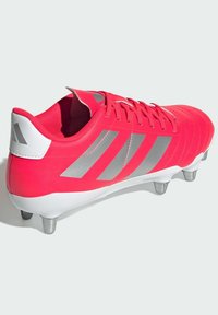 Scarpone da calcio con tomaia sintetica rosa brillante, tre strisce argento, tallone bianco e tacchetti metallici argento per la trazione.