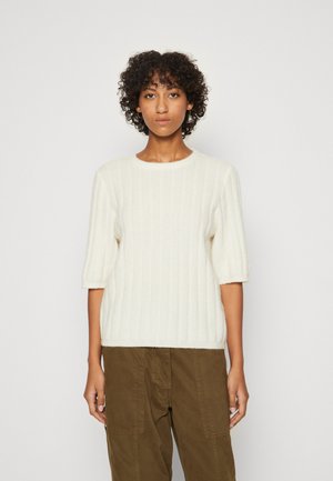Cream-colored ribbed sweater with short sleeves and a round neckline, made from soft fabric, paired with olive green pants.