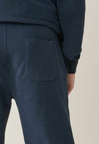 Marineblaue Sweatpants mit weicher Textur, die eine einzelne aufgesetzte Tasche und einen elastischen Bund aufweisen, von hinten aufgenommen.