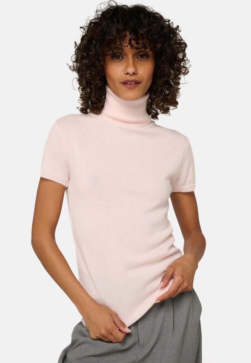Pull en col roulé à manches courtes de couleur rose clair, fabriqué dans un tissu doux et léger avec une texture lisse. Présente un design ajusté et un col côtelé.