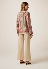 Bluză fluidă, cu model în culori pastelate, cu mâneci lungi. Asortată cu pantaloni largi de culoare crem și sandale cu toc.