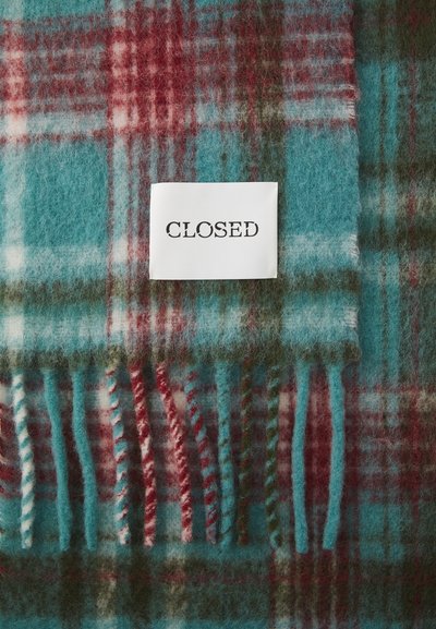 Rudeblanket i teal, rød og grøn med frynset kanter. Et hvidt mærke med "CLOSED" er fastgjort. Blødt, tekstureret materiale.