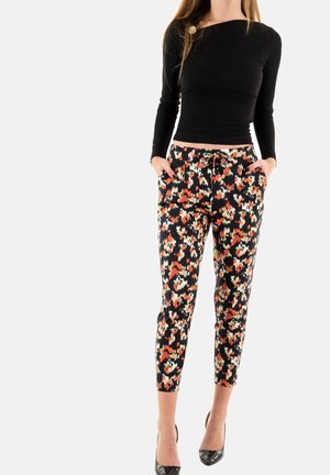 Woman wearing black long-sleeve top and black cropped pants with orange, white, and red floral print, standing with hands in pockets.