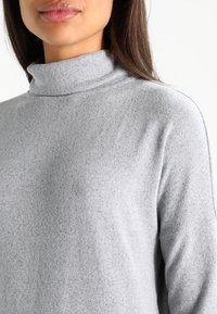 Grå polotröja med en mjuk textur, avslappnad passform och en enkel design som framhäver en slät halsringning och subtilt mönster i tyget.
