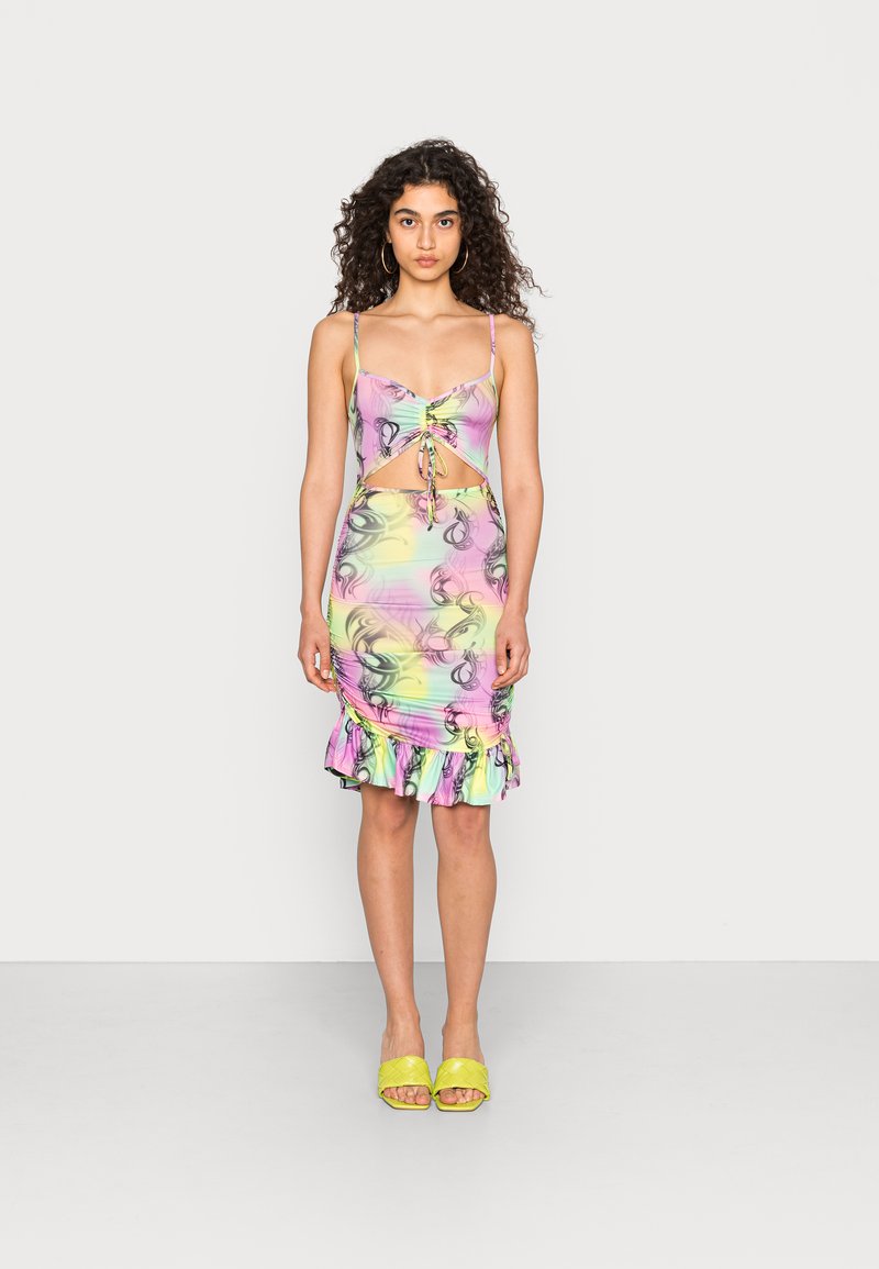 Vestido sem mangas, em tons pastel, com padrão floral, textura franzida, detalhe recortado e bainha com volantes. Modelo calça sandálias de salto amarelas.