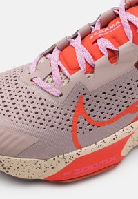 Chaussures de running Nike ZoomX présentant un upper en mesh violet clair avec des accents orange, des lacets roses et une semelle beige marbrée.