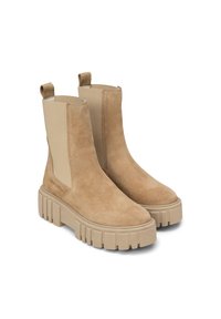 Bottines en suede beige avec des panneaux élastiques sur les côtés et une semelle en caoutchouc épaisse, présentant une texture lisse et un design minimaliste.