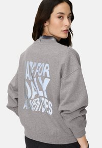 Grijze trui met ronde hals, oversized pasvorm en de tekst "MADE FOR DAILY ADVENTURES" in lichtblauw op de achterkant. Zacht, gestructureerd stof.