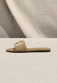 Μπεζ πλατφόρμα σανδάλι με φαρδιά λουρί και μικρή χρυσή αγκράφα σε ουδέτερη επιφάνεια με απαλές σκιές.