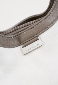 Witte textuur leren tas met een gladde grijze rits en een reliëf zilveren merklabel. Het ontwerp heeft een ronde bovenkant.