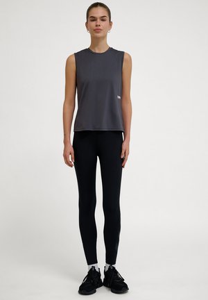 Ärmlös grå träningströja med rund hals, i kombination med svarta leggings och svarta sneakers. Slät tyg med en subtil lyster.
