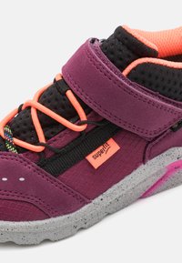 Fialová sportovní obuv s prodyšným svrškem a šedou skvrnitou podešví. Obsahuje oranžové tkaničky, suchý zip a vícebarevné akcenty.