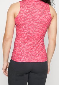 Hihaton paita kirkkaan vaaleanpunaisena, jossa on valkoinen abstrakti kuvio, korkea kaulus ja vartalonmyötäinen malli, joka kerää hieman vyötäröltä.