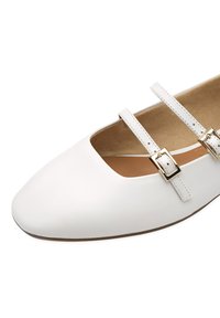 Ballerine en cuir blanc avec un bout arrondi, dotée de deux brides réglables avec quincaillerie dorée, d'un rembourrage intérieur et d'une finition lisse.