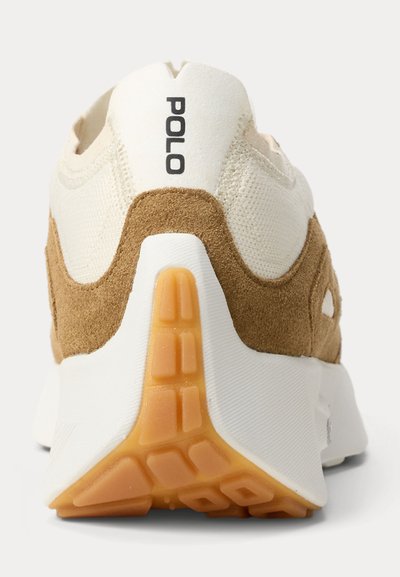 Hátsó nézet egy bézs és barna színű, velúr Polo sportcipőről, fehér talppal és narancssárga gumi talprészlet részlettel.