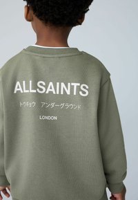 Oliivinvihreä collegepaita, jossa on ribbineulottu rakenne ja valkoiset painetut tekstit: "ALLSAINTS", japanilaisia merkkejä ja "LONDON" selässä.