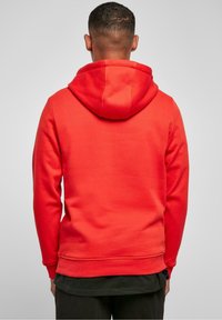 Sudadera roja con un bolsillo tipo canguro, capucha con cordón y puños acanalados. Fabricada con tela suave, presenta una textura lisa y un color sólido.