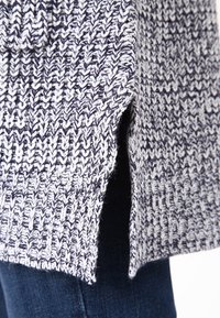 Pletený svetr v námořnické modři a bílé barvě s texturovaným vzorem. Detail s bočním rozparkem. Měkký materiál, pravděpodobně vyrobený z vlny nebo vlněné směsi.