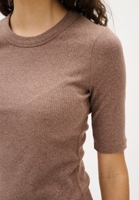Ruskea raitapaita lyhyillä hihoilla, jossa on pyöreä pääntie, vartalonmyötäinen muoto ja tekstuuri, jossa on hienoinen kiilto.