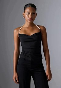 Top negro de haltera con tela fruncida y tirantes adornados con perlas, que presenta un escote corazón y una textura suave. Se lleva con pantalones negros.