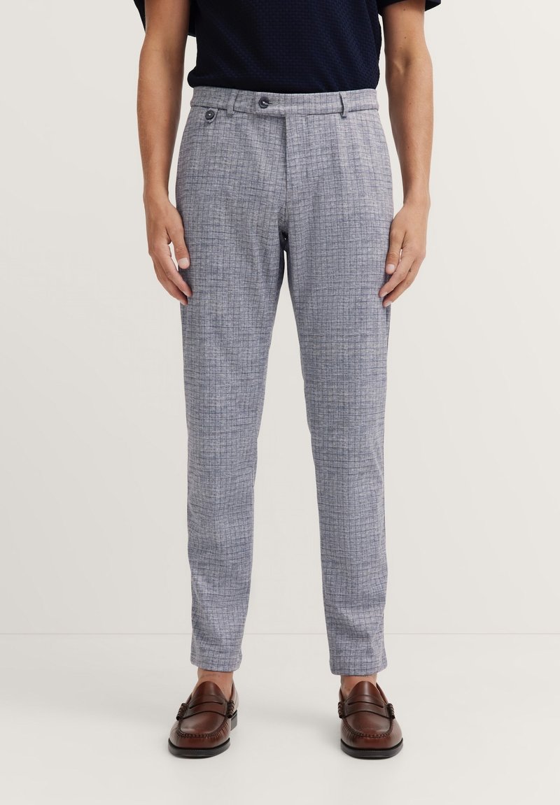 Grau karierte Hosen aus leichtem Stoff, mit taillierter Passform, zwei vorderen Knöpfen und seitlichen Taschen. Getragen mit braunen Slippern.