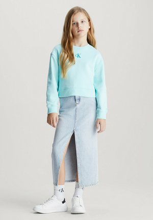 Sudadera corta de color azul claro con cuello redondo, combinada con una falda maxi de mezclilla con una abertura frontal. Zapatillas blancas y calcetines con logo completan el look.