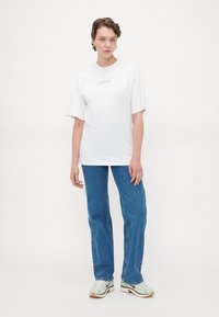 Vit bomullströja med "FEMME" tryckt i ljusblått. Matchad med blå raka jeans och ljusa sneakers. Enkel design.