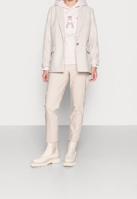 Blazer gris claro sobre una sudadera con capucha rosa pálido con un estampado gráfico, combinado con pantalones ajustados beige y botas de suela gruesa color crema.