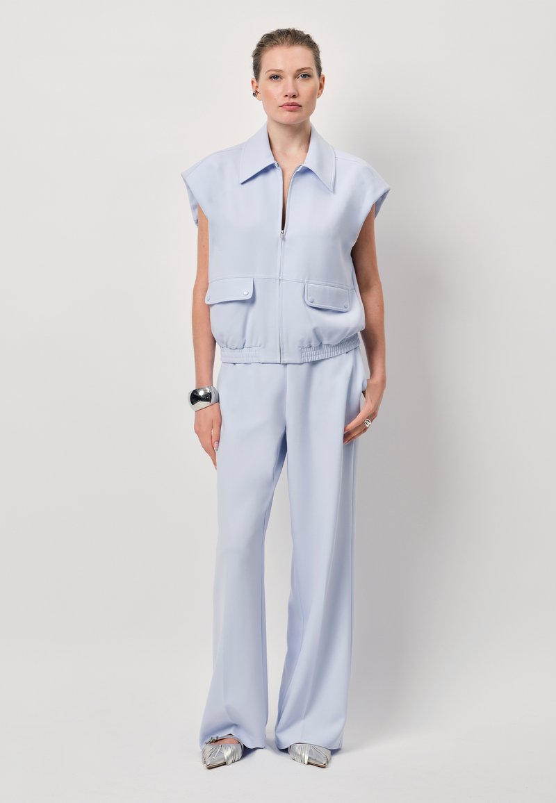 Lichtblauwe cropped jas met korte mouwen, ritssluiting en twee voorzakken, gecombineerd met bijpassende loszittende broeken en metallic schoenen.