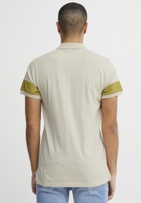 Lys beige polo-skjorte med korte ermer og grønne detaljer ved mansjettene. Myk stoff med en jevn tekstur og rett kant.