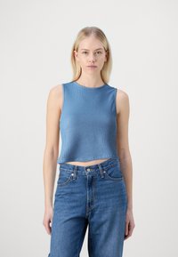 Lyseblå ribbestrikket tanktop med rund hals, cropped lengde og uten ermer, i kombinasjon med høytliv blå denim jeans.