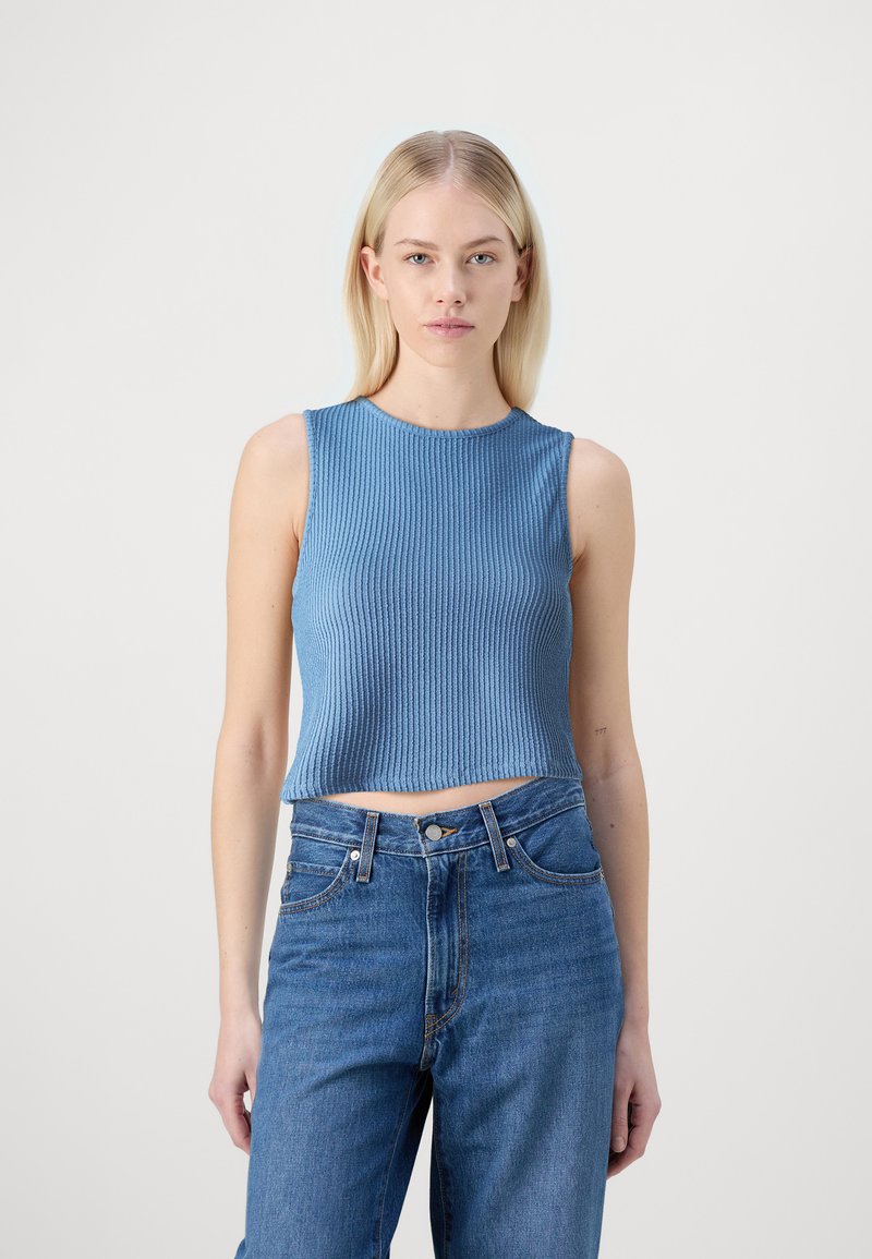 Lyseblå ribbestrikket tanktop med rund hals, cropped lengde og uten ermer, i kombinasjon med høytliv blå denim jeans.