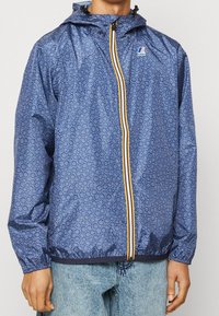 Blå mønstret jakke med hætte, som har en lynlåslukning med en gul stribe, elastiske manchetter og et elastisk bånd i taljen.