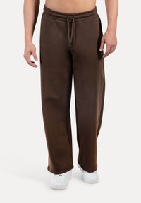 Pantaloni della tuta in misto cotone marrone con vestibilità rilassata, girovita elasticizzato e dettaglio con coulisse, abbinati a sneaker bianche.