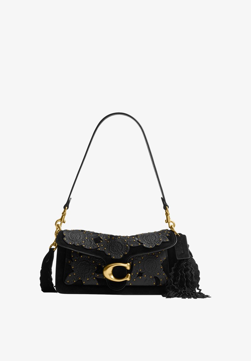 Sac à bandoulière en cuir noir avec des clous dorés, des motifs floraux découpés, une grande fermeture dorée et un pompon décoratif noir sur le côté.