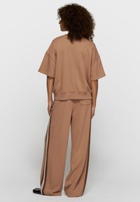 Sweat-shirt marron et pantalon large assorti avec des bandes blanches sur les côtés. Texture douce, coupe décontractée et col rond.