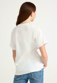 Hvid bomulds T-shirt med korte ærmer, afslappet pasform og rund halsudskæring. Båret med blå jeans med kontrastsyninger på lommerne.