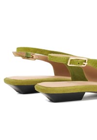 Green suede sandals featuring a narrow ankle strap with gold hardware, a sleek black heel, and a textured beige insole.