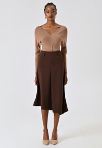 Top in maglia marrone con scollo a V e dettaglio dei bottoni, abbinato a una gonna fluida marrone che arriva sotto il ginocchio e tacchi alti nude.