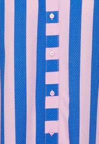 Chemise rayée avec des rayures verticales bleues et roses alternées, en tissu texturé, et une rangée de boutons roses le long de la patte de boutonnage.