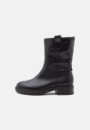 Botte en cuir noire mi-mollet à bout rond, petit talon bloc, languette latérale et coutures visibles sur un fond uni.
