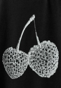 Crni materijal sadrži grafički otisak dviju stiliziranih višnje, obrubljenih svijetlom bojom s raskošnim uzorcima koji podsjećaju na čipku ili mrežu.