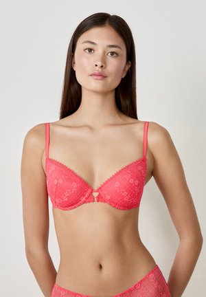 Soutien-gorge en dentelle corail avec un décolleté plongeant, des bretelles ajustables, des motifs floraux et un petit détail en forme de trou de serrure au centre.
