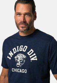 Mørkeblå bomulds t-shirt med et hvidt grafisk tryk af en brølende tiger og teksten "INDIGO DIV. CHICAGO" i fede bogstaver. Behagelig pasform.
