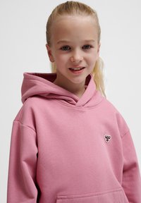 Różowa bluza z kapturem z przednią kieszenią i sznurkiem do regulacji; na lewej części piersi znajduje się małe haftowane logo. Materiał mieszany bawełniany.