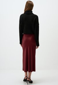 Maglione nero a maglia con collo alto, abbinato a una gonna midi in satin bordeaux, con una texture liscia e un orlo svasato. Sandali neri con tacco alto.