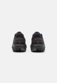 Schwarze Sportschuhe mit einem strukturierten Mesh-Obermaterial, runder Zehenform und gepolstertem Sohlen. Merkmale sind auffällige Nahtmuster an der Ferse.