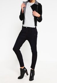 Svarta slim fit-jeans med en mjuk textur, i kombination med en grå kortärmad tröja och en svart jacka med dragkedja och grå krage. Avslutat med svarta klackade ankelstövlar.