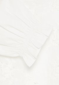 Tissu blanc avec des détails de poignet élastique froncé sur un fond à motif floral texturé.