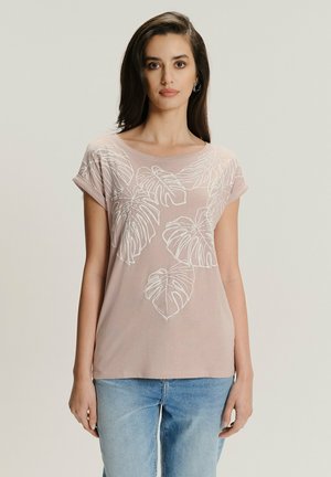 Jasnoróżowa koszulka z krótkimi, zawiniętymi rękawami, z białymi haftowanymi wzorami liści monstera na przodzie. Miękka tekstura materiału.